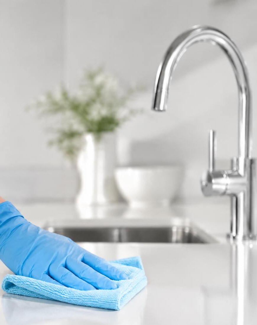 Gloved hand wiping a spotless white kitchen benchtop